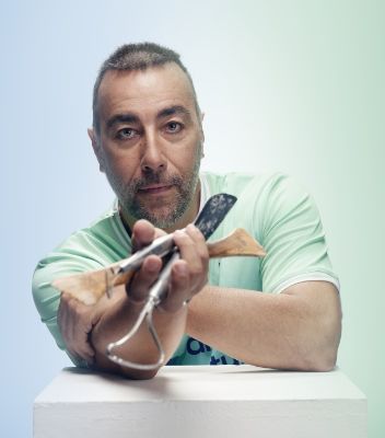 Lorenzo Quinn wearing his green and blue Team Century jersey and extending his hand holding sculpting tools toward the camera.