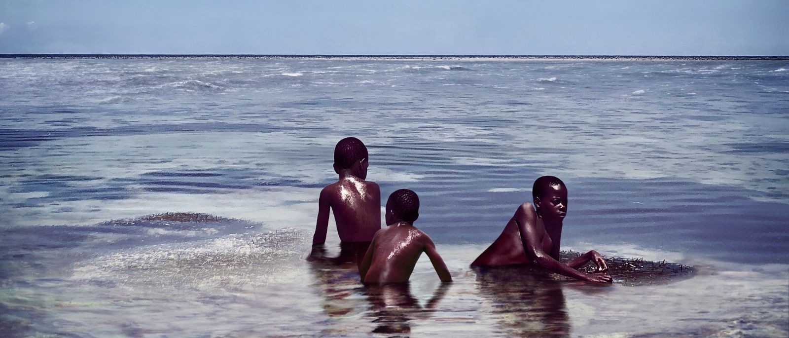 Three boys sitting on the last remaining piece of land surrounded by ocean. 