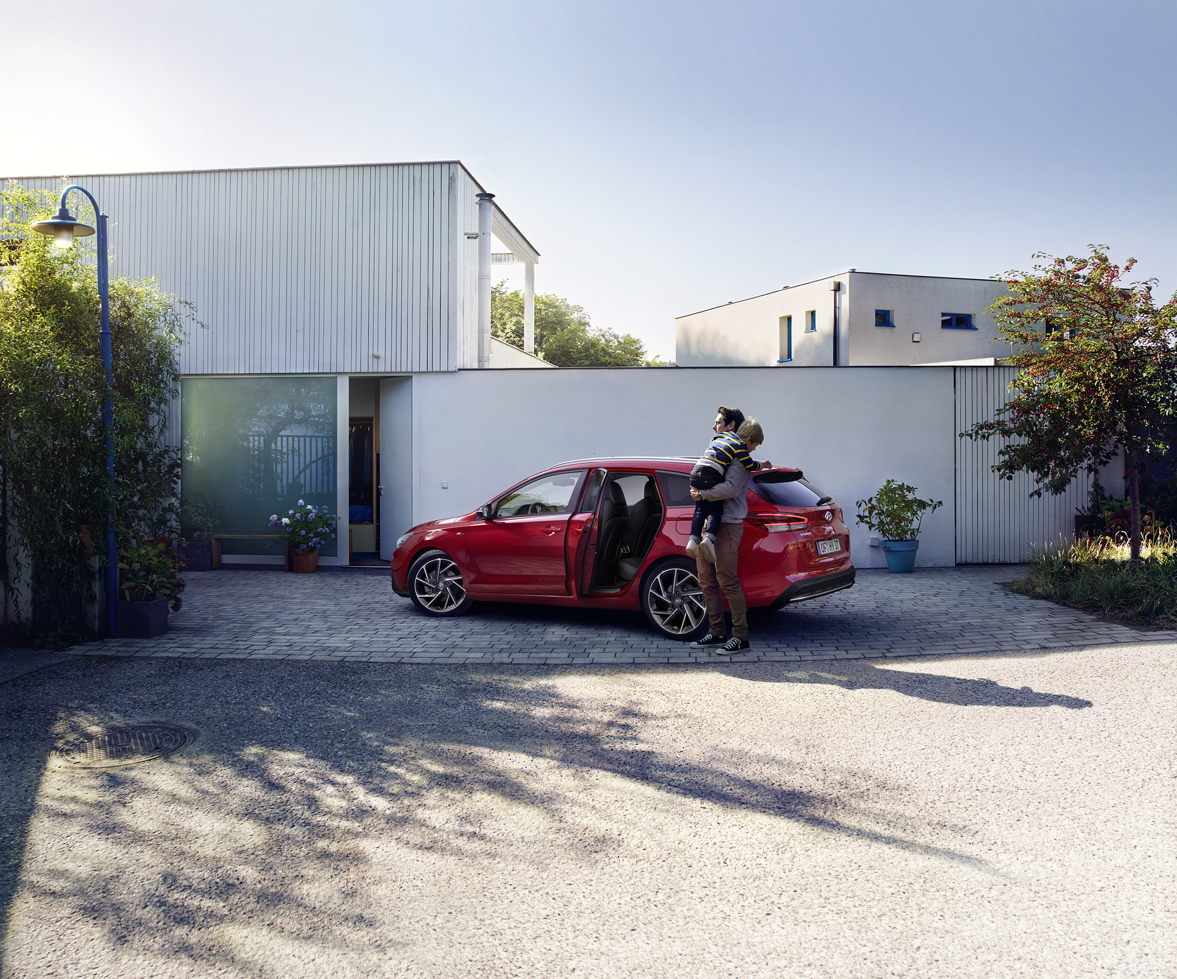 Ein Mann mit Kind auf der Schulter vor einem Haus und einem parkenden Hyundai i30 Kombi.