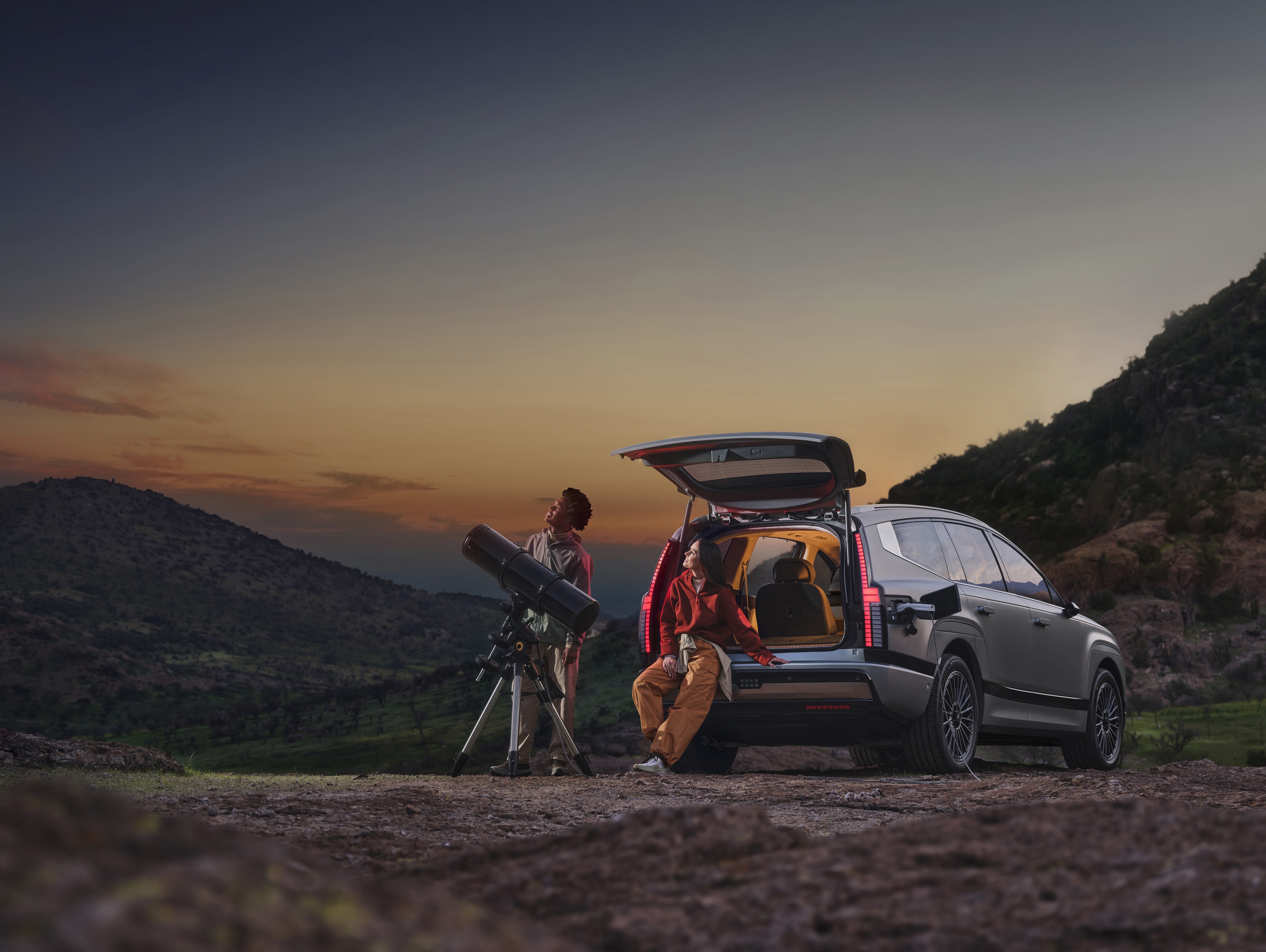 Parked IONIQ 9 with tailgate open using V2L to power a telescope for stargazing.